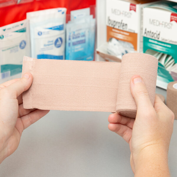 A hand holding a roll of Medi-First elastic bandages.