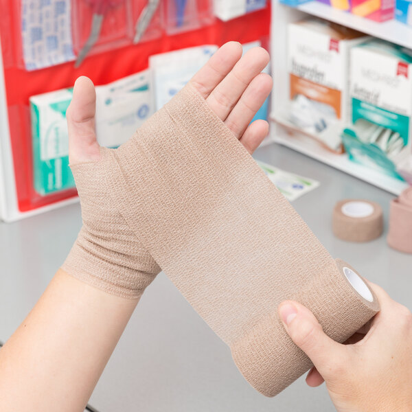 A hand holding a roll of Medi-First self adhesive bandages.