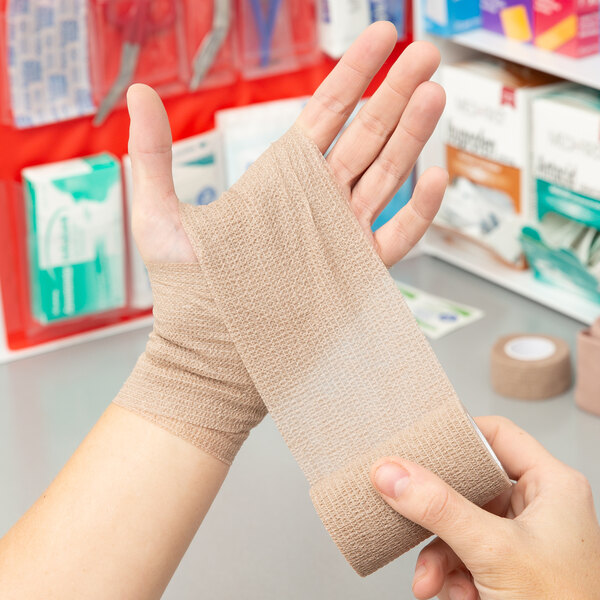 A person holding a roll of Medi-First self adhesive wrap.
