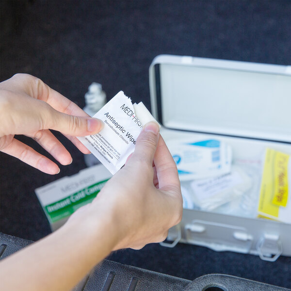 A person holding a small white box of Medique first aid supplies.