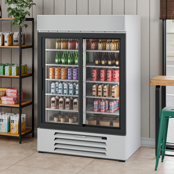 A white two-section glass door merchandiser refrigerator filled with various beverages and food items.