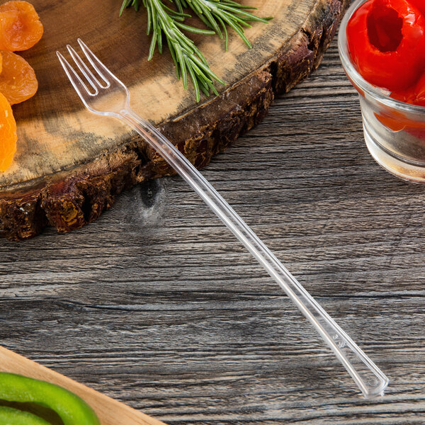 A Fineline clear plastic cocktail fork on a wood surface.