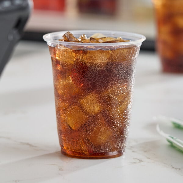 A clear 12 oz. compostable plastic cold cup filled with iced soda.