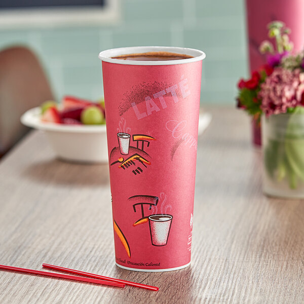 A pink Solo paper hot cup on a table with a bowl of fruit.