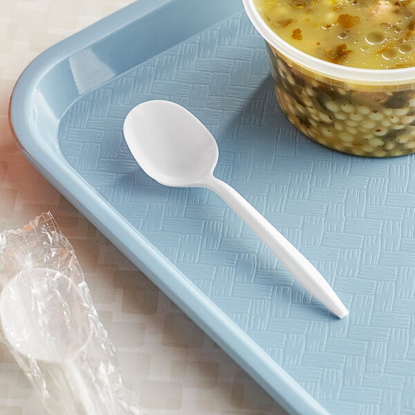 A white plastic spoon next to a bowl of soup.