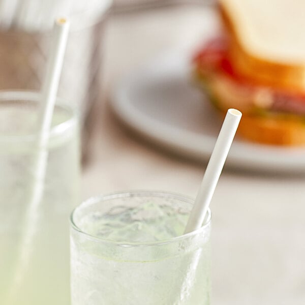 A glass of green drink with a white EcoChoice paper straw in it next to a sandwich.