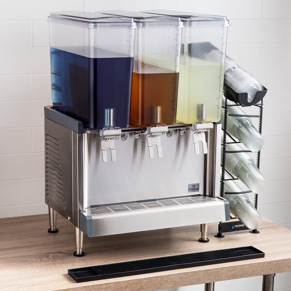 A black rectangular Crathco Simplicity bowl kit on a wood surface with three containers of different colored liquid.