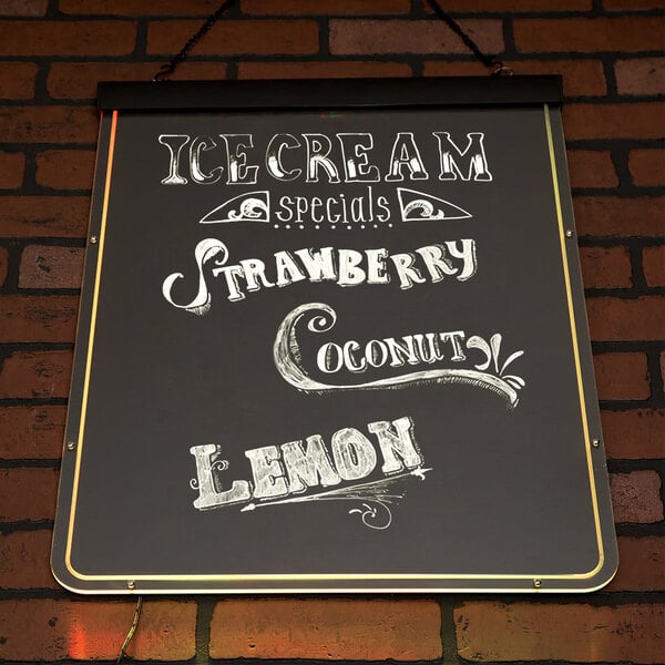 A white Aarco lighted write-on menu board sign on a brick wall advertising ice cream and strawberries.