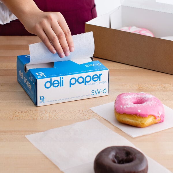 A hand using Durable Packaging deli wrap paper to pick up a pink donut with sprinkles.