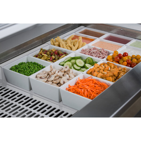 A white Tablecraft cast aluminum drop-in cold well with food in it.