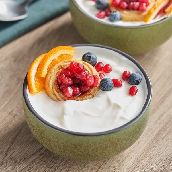 A bowl of plain Greek yogurt topped with orange slices, a pastry, pomegranate seeds, and blueberries.