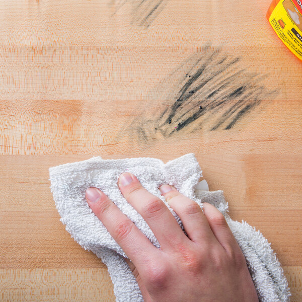 A person using Goo Gone Pro-Power to clean a wooden table.