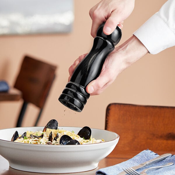 A hand using an Acopa wooden pepper mill to add pepper to a bowl of pasta.