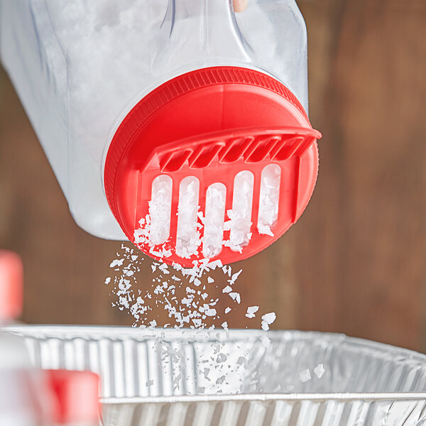 A hand pouring salt into a red spice container with a red shaker lid.