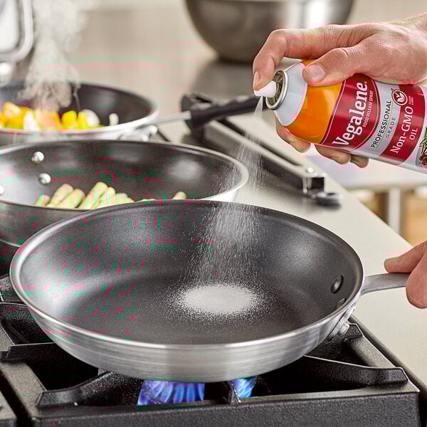 A hand using Vegalene Non-GMO Food Release Spray to coat a pan.