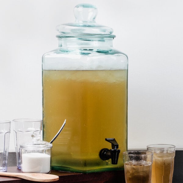 A Cal-Mil glass beverage dispenser filled with clear liquid and glasses.