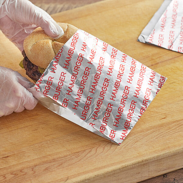 A person in gloves putting a hamburger in a Carnival King paper bag.