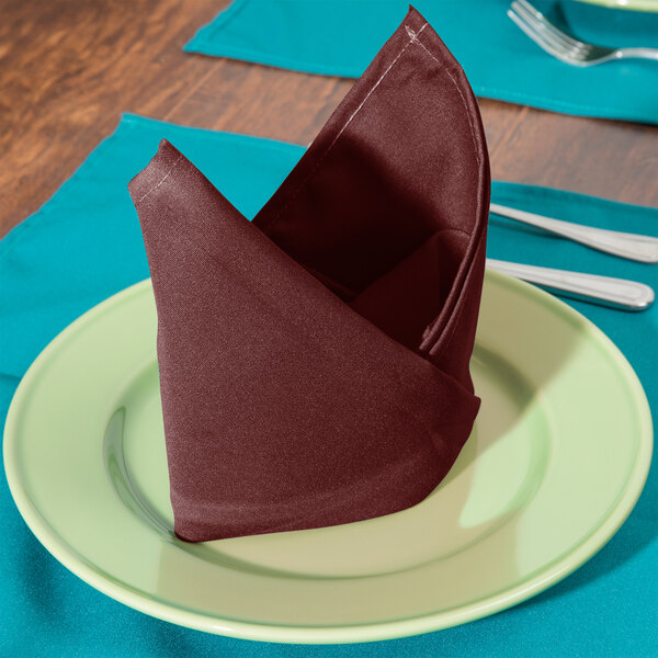 A folded burgundy Intedge cloth napkin on a plate.