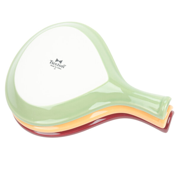 An assorted stack of Tuxton China Fry Pan Servers in green, yellow, and other colors.