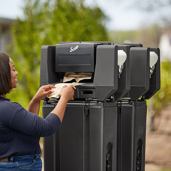 A woman putting a napkin in a black Cambro multi fold towel dispenser.