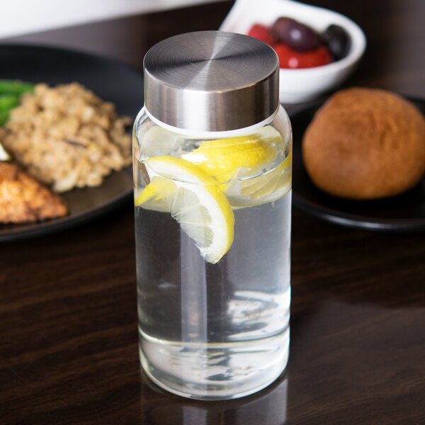 A Libbey glass bottle with metal lid filled with water and lemon slices on a black surface.