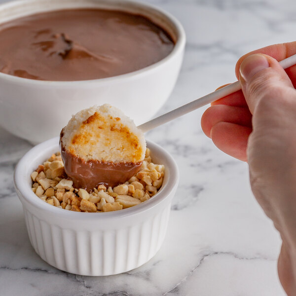 A hand holding a Paper Lollipop Stick with a chocolate covered dessert in a bowl of chocolate.