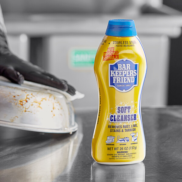 A gloved hand uses Bar Keepers Friend all purpose soft cleanser to clean a dirty metal surface.