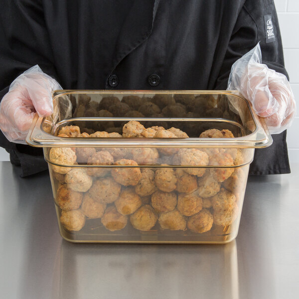 A person holding a Carlisle amber high heat food pan drain tray with food inside.