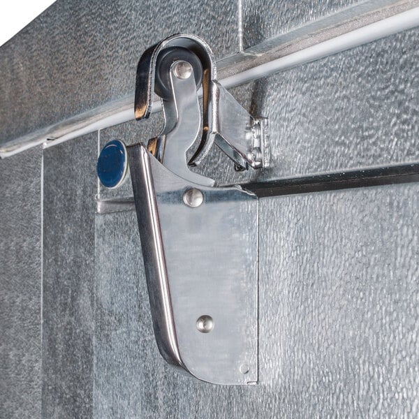 A metal latch mechanism attached to the door of an outdoor walk-in cooler.