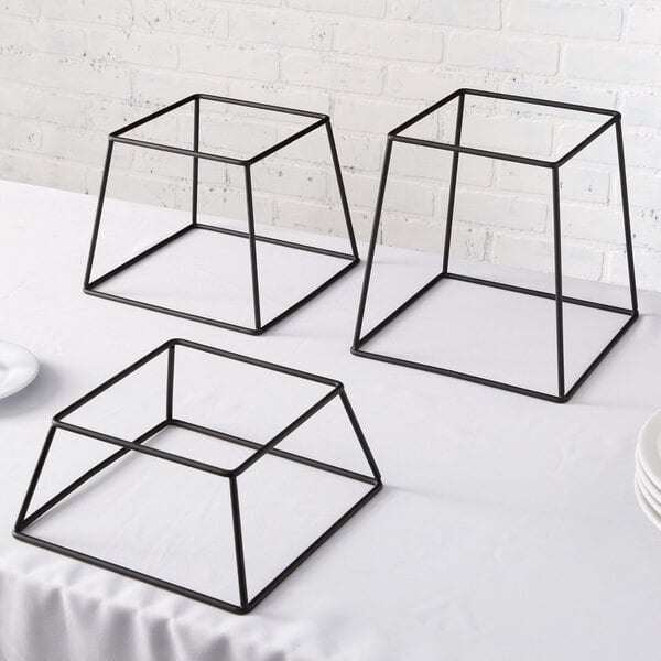 A set of three black metal Acopa display stands on a table.