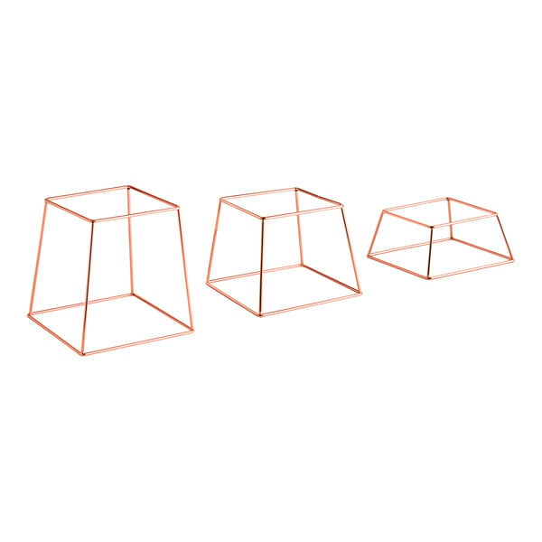 A set of three square rose gold metal display stands in varying sizes.