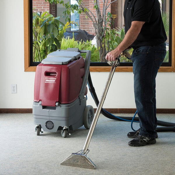 A man using a Minuteman Rush 100 carpet extractor to clean a carpet.