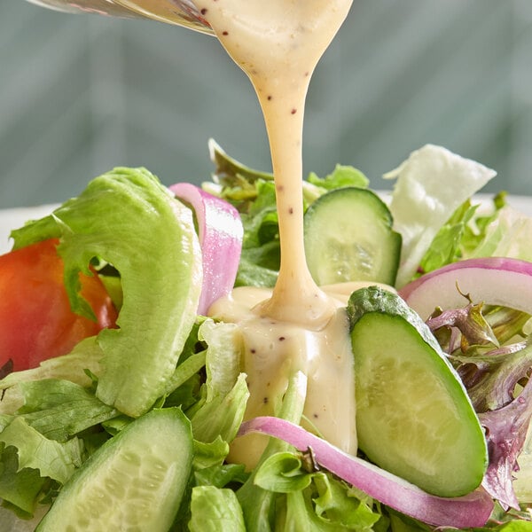 A fresh salad with cucumbers, lettuce, tomatoes, and onions being topped with creamy poppyseed dressing.