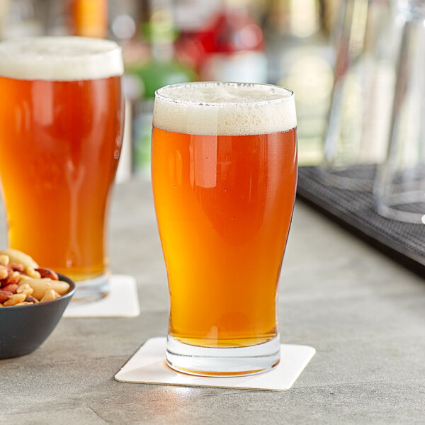 Two Acopa pub glasses of beer on a table with a bowl of nuts.