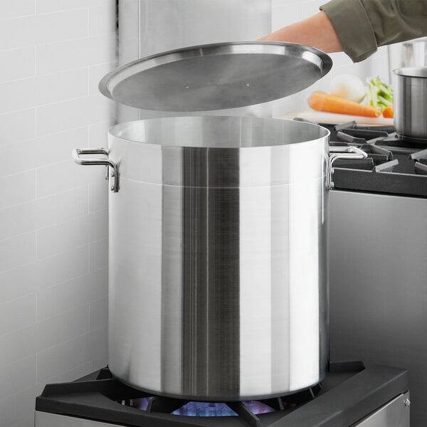 A person using a Choice large silver stock pot with a lid on a stove.