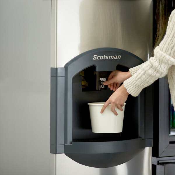 A person putting a cup into a Scotsman ice machine.