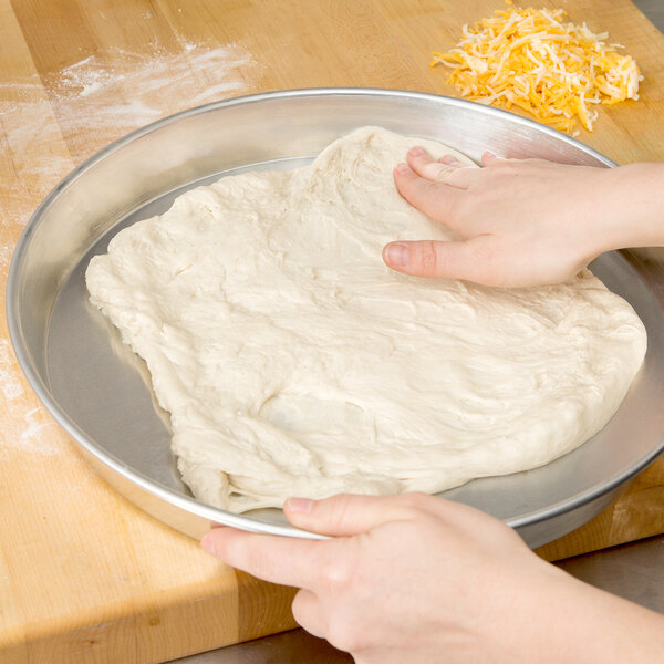 A person's hand rolling pizza dough in an American Metalcraft tapered pizza pan.