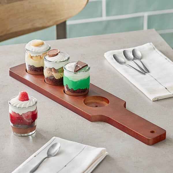 An Acopa mahogany flight paddle with rounded tasting glasses holding desserts on a table.