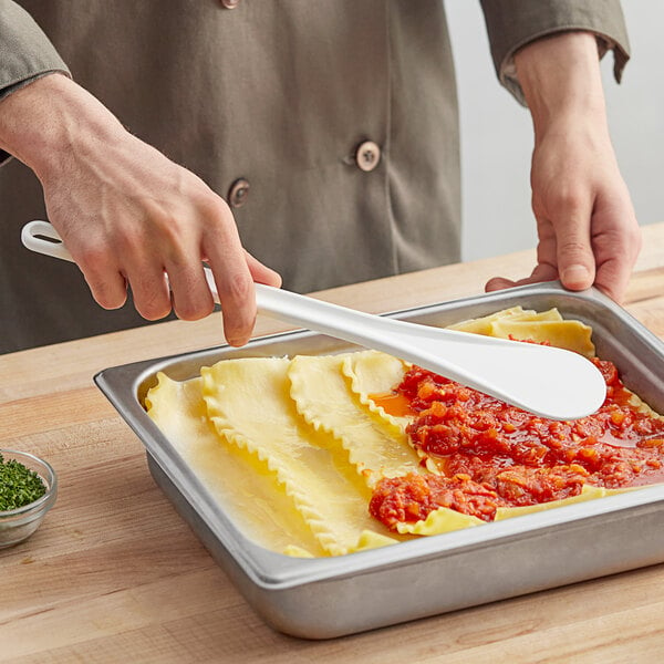 A person holding a white Mercer Culinary High Temperature Spootensil over a plate of pasta.