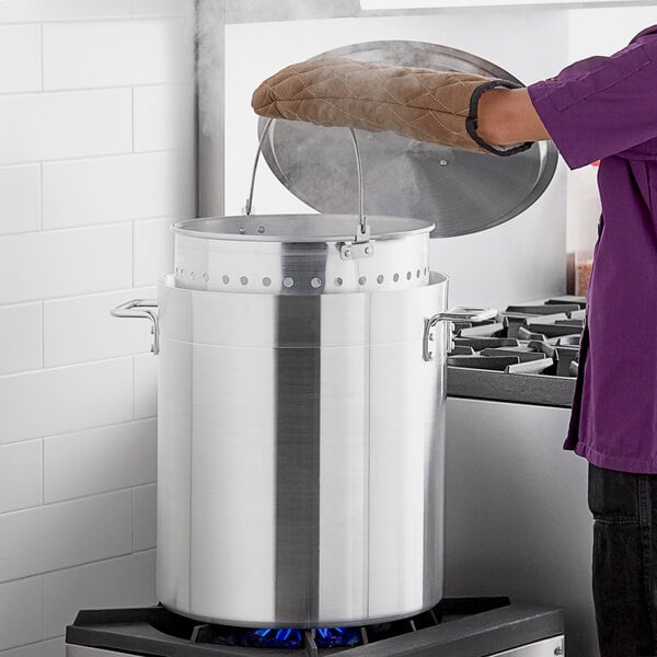 A person in a brown glove uses a Choice aluminum stock pot to cook.