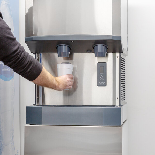 A person using a Scotsman water dispenser to fill a cup with water.