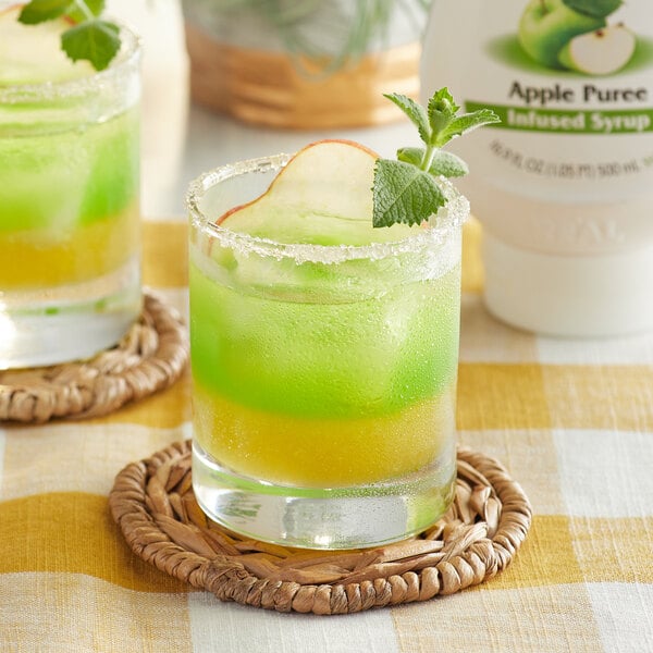 A glass of green and yellow liquid with a slice of apple on top with a bottle of Real Apple Puree Infused Syrup.