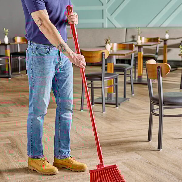 A man using a Carlisle Sparta red fiberglass broom handle to sweep a floor.