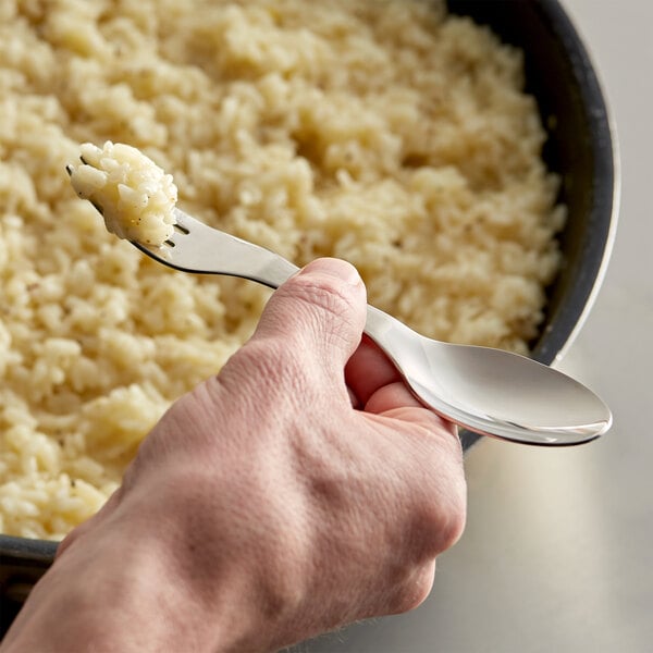 A hand holding a Mercer Taste stainless steel fork with a spoon in front of a bowl of rice.