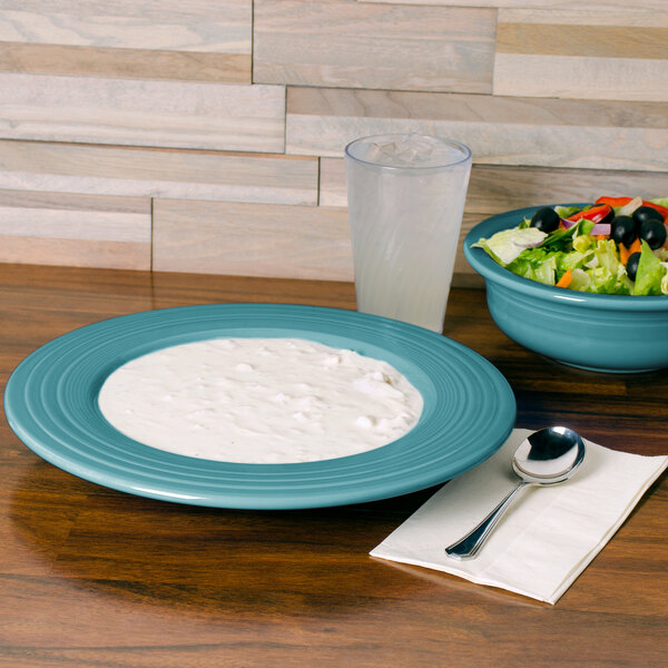 A Fiesta turquoise china pasta bowl filled with salad on a table with a glass of water.