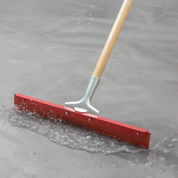 Red gum rubber floor squeegee pushing water to a drain