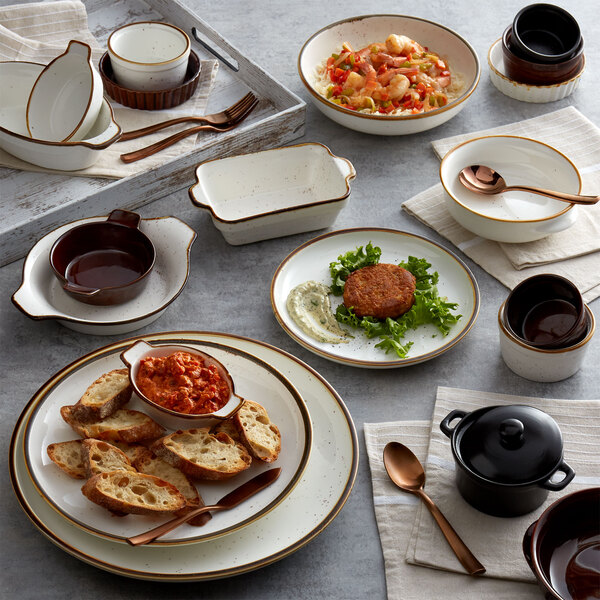 A table with white plates, bowls, and Acopa Keystone brown stoneware ramekins on it.