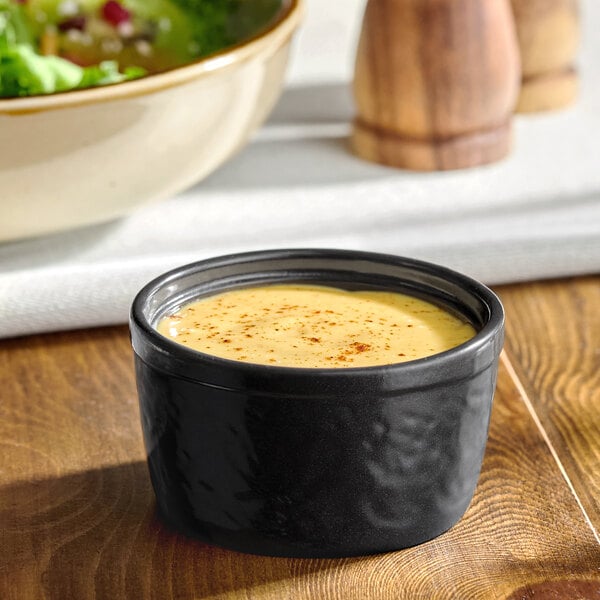 A black stoneware ramekin filled with a creamy sauce or dressing.
