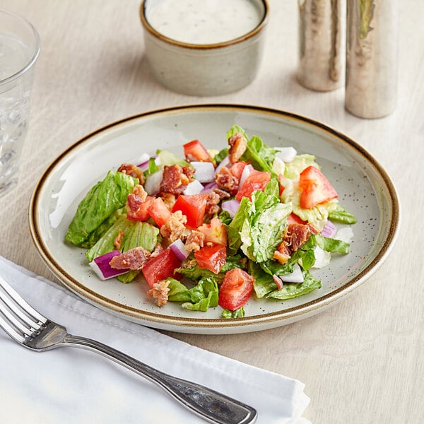 An Acopa vanilla bean stoneware coupe plate with a salad of bacon, lettuce, and tomatoes on a table