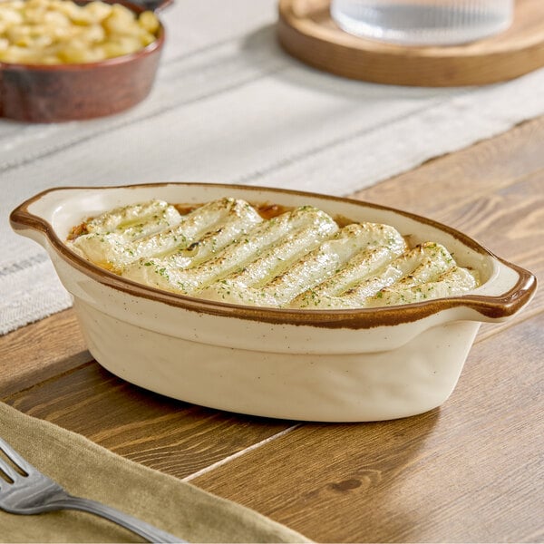 An oval-shaped vanilla bean porcelain baker or casserole dish with a brown rim, shown filled with baked food.